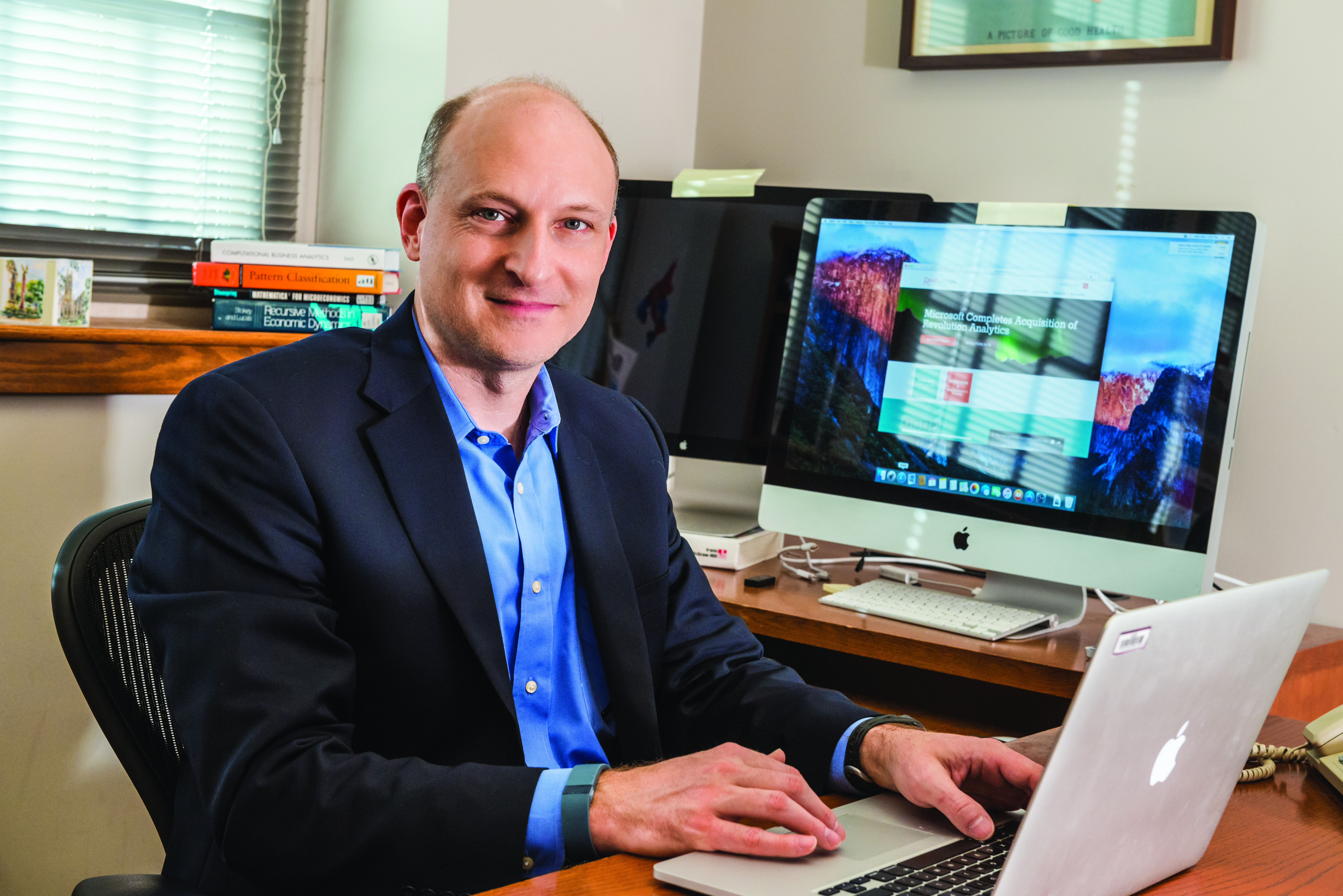 Sam Ransbotham in his office with a laptop, smiling at the camera